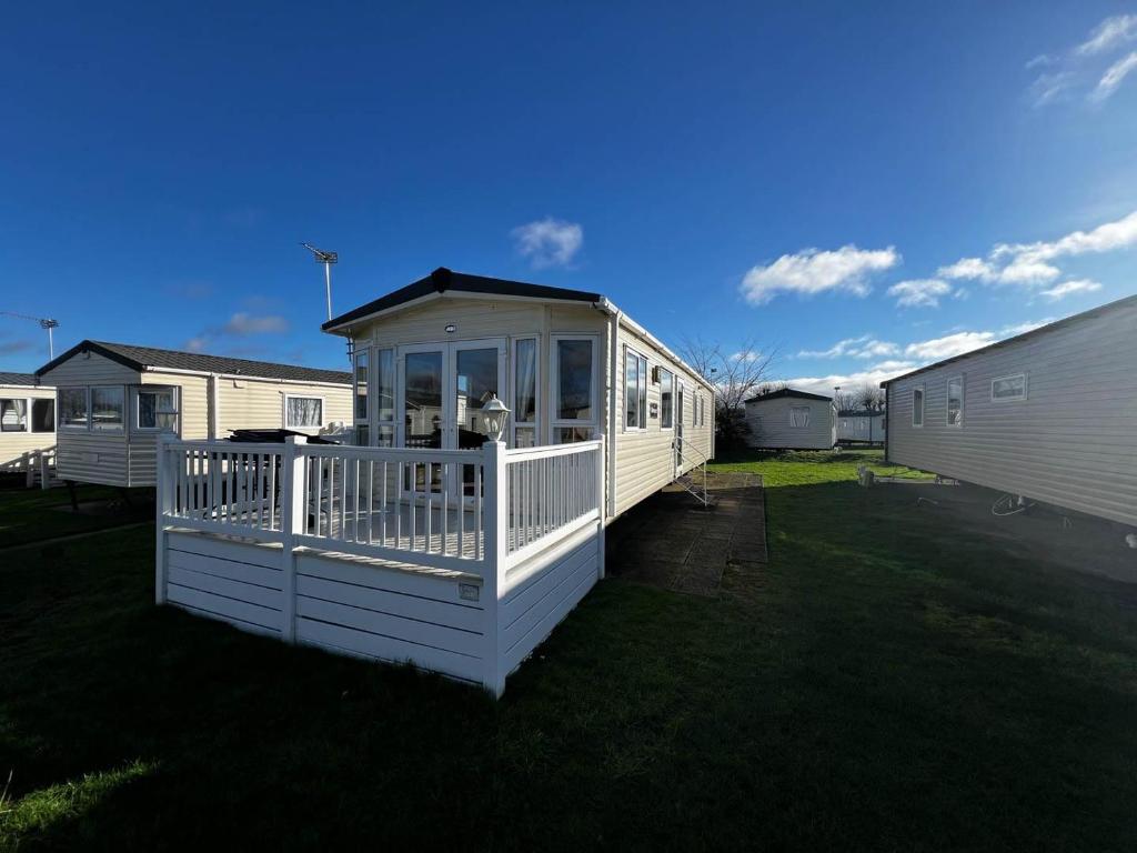 een wit huis met een veranda op het gras bij Lovely Caravan With Decking At Cherry Tree Holiday Park In Norfolk Ref 70528c in Great Yarmouth