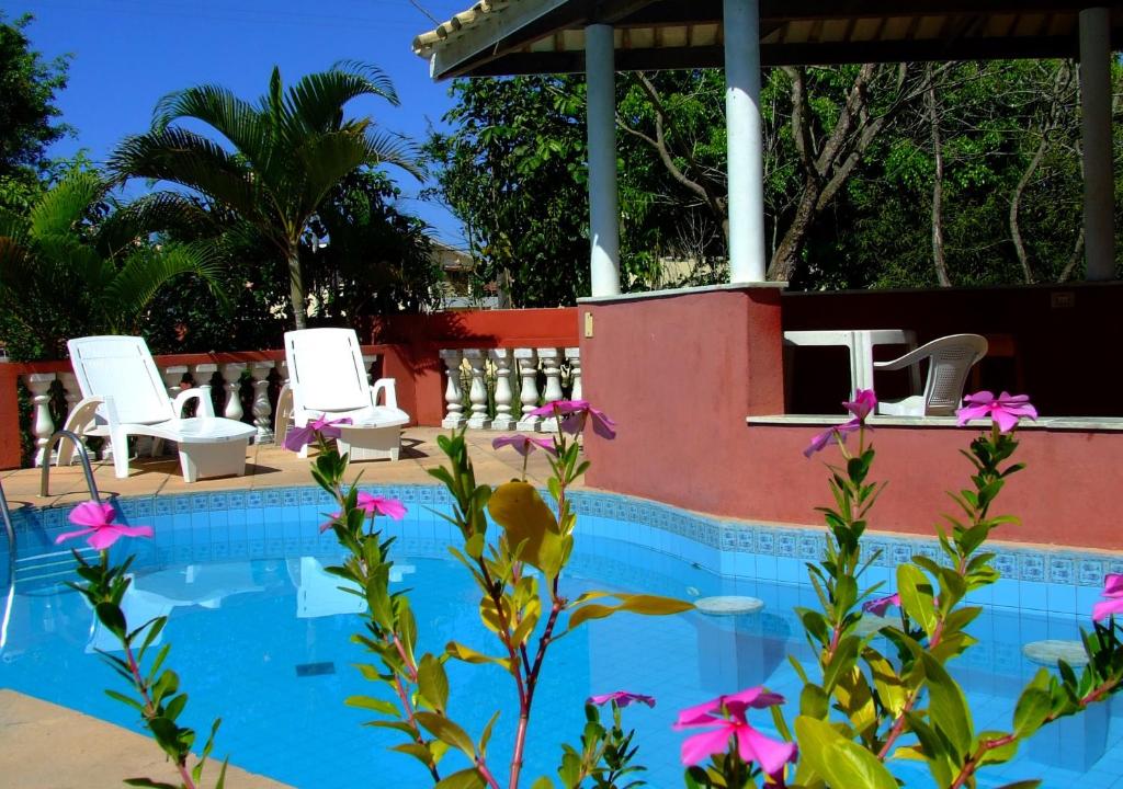 a swimming pool with two white chairs and pink flowers at Porto Verano Residence in Porto Seguro