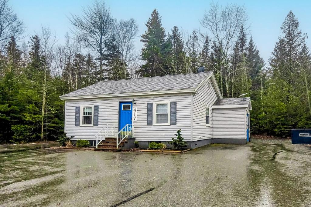 ein weißes Haus mit blauer Tür auf einem Parkplatz in der Unterkunft Blue Button Cottage in Gouldsboro