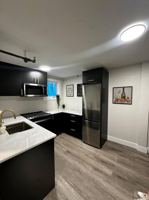 a kitchen with black cabinets and a stainless steel refrigerator at Quaint Queen Suite Central HFX in Halifax