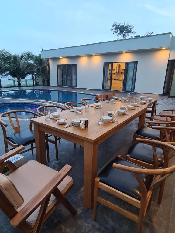 ファンティエットにあるLang Chai Beachfront Villa Phan Thietのプールサイドの長い木製テーブルと椅子