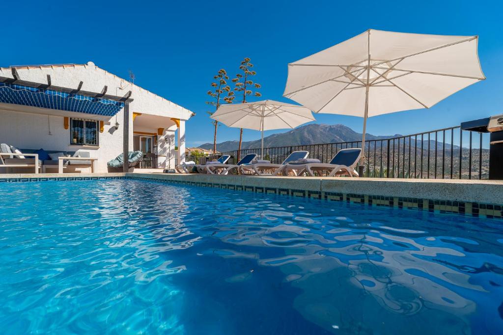 une piscine avec des parasols et des chaises ainsi qu'une maison dans l'établissement Villa Maroma, à Viñuela