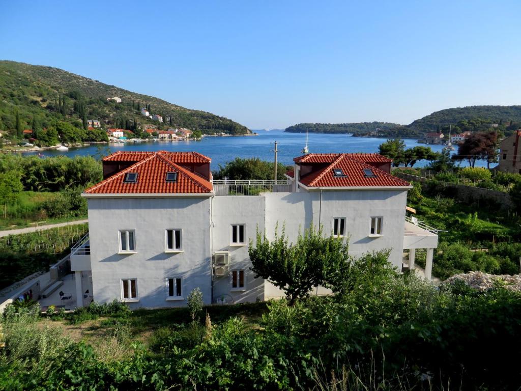 a white house with red roofs on a hill with a lake at Guest House Kukuljica 2 in Zaton