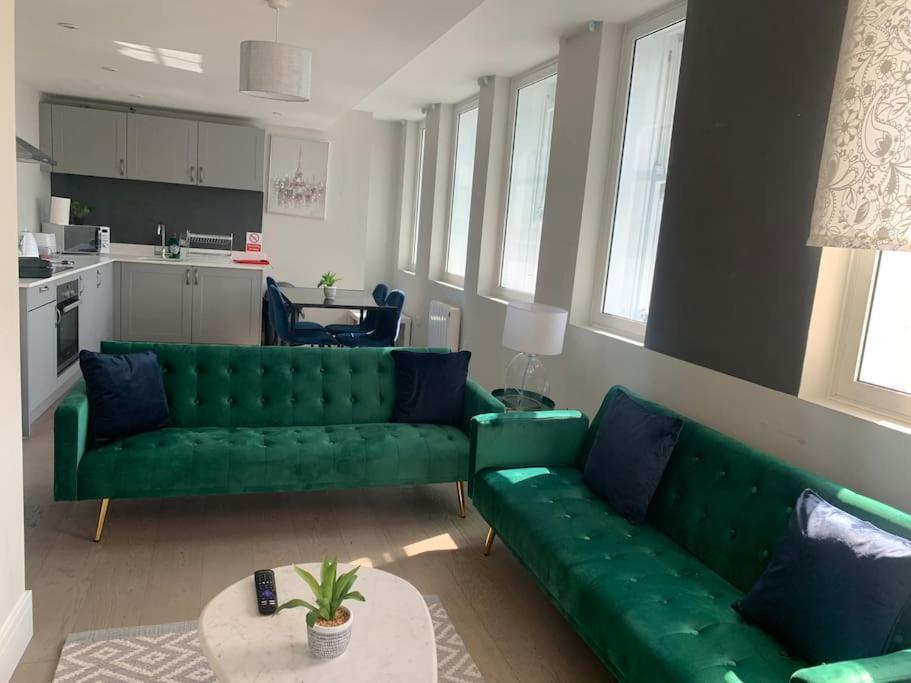 a living room with a green couch and a kitchen at Two bedroom, modern spacious apartment. in Brentwood