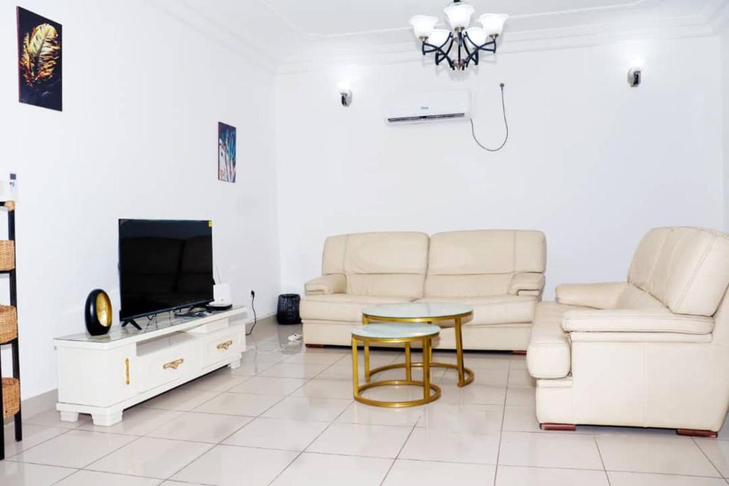 a living room with white furniture and a tv at Home By Dina'Sty in Yaoundé