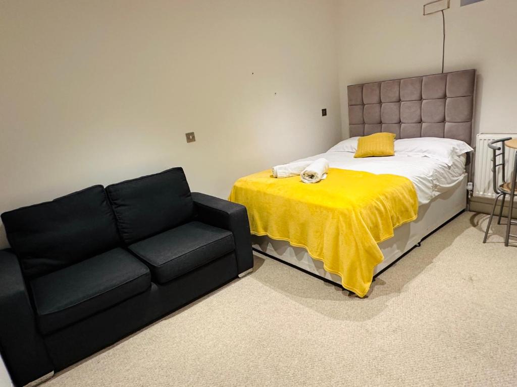 a bed with a yellow blanket next to a black couch at Cute and Comfy Studio in King’s Cross in London