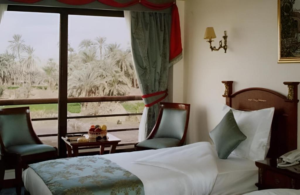 a bedroom with a bed and two chairs and a window at NILE CRUISE LUXOR & AsWAN نايل كروز الاقصر و اسوان in Aswan