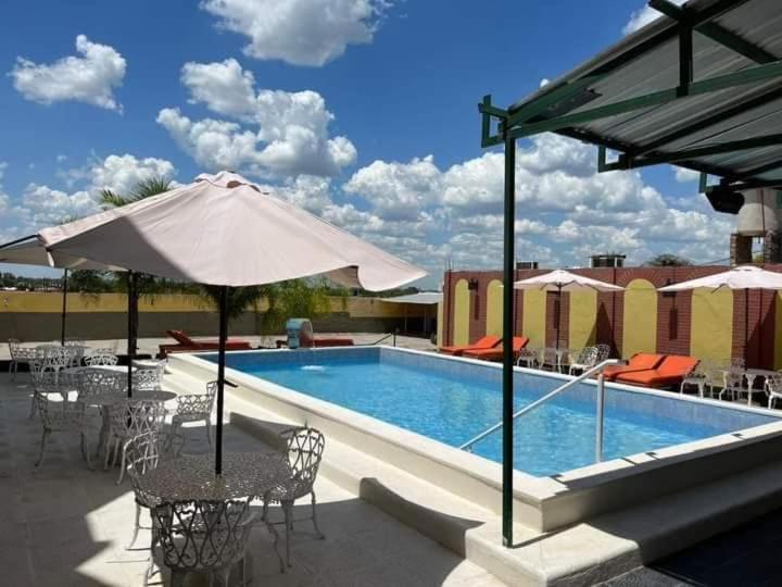 a swimming pool with tables and chairs and an umbrella at Hotel Santander in Termas de Río Hondo