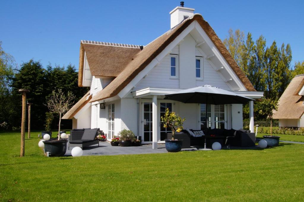 a white house with chairs and an umbrella at Golden Wellness Villa Noordwijk in Noordwijk