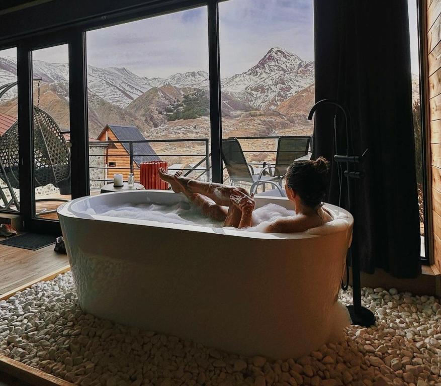 a man laying in a bath tub with a mountain view at Kazbegi Story in Stepantsminda