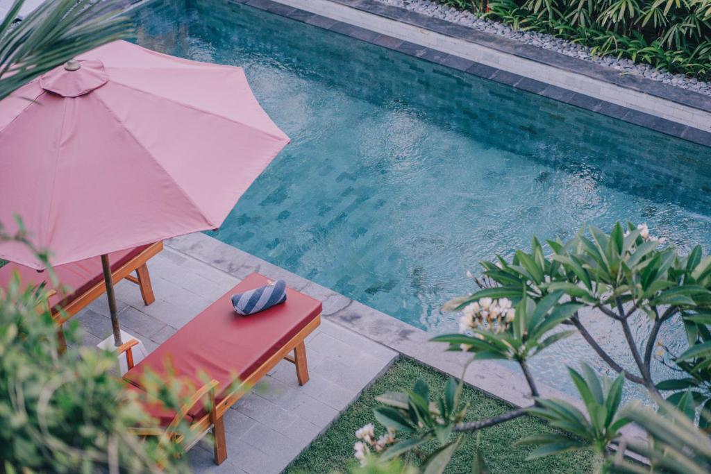 an umbrella and a chair next to a swimming pool at Cucukan Beach Guest House in Gianyar