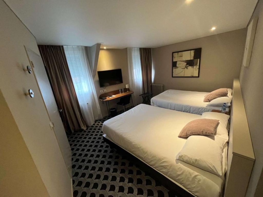 a hotel room with two beds and a desk at Brit Hotel Les Voyageurs in Loudéac