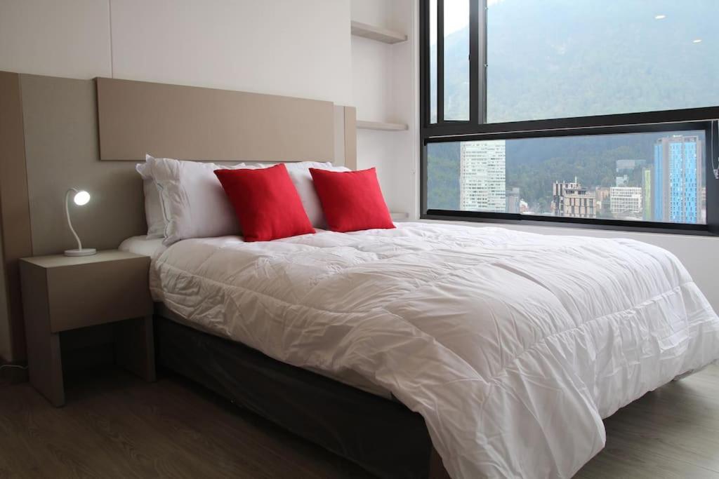 16 Torre Barcelona Apartment, City Center في بوغوتا: غرفة نوم بسرير ومخدات حمراء ونافذة