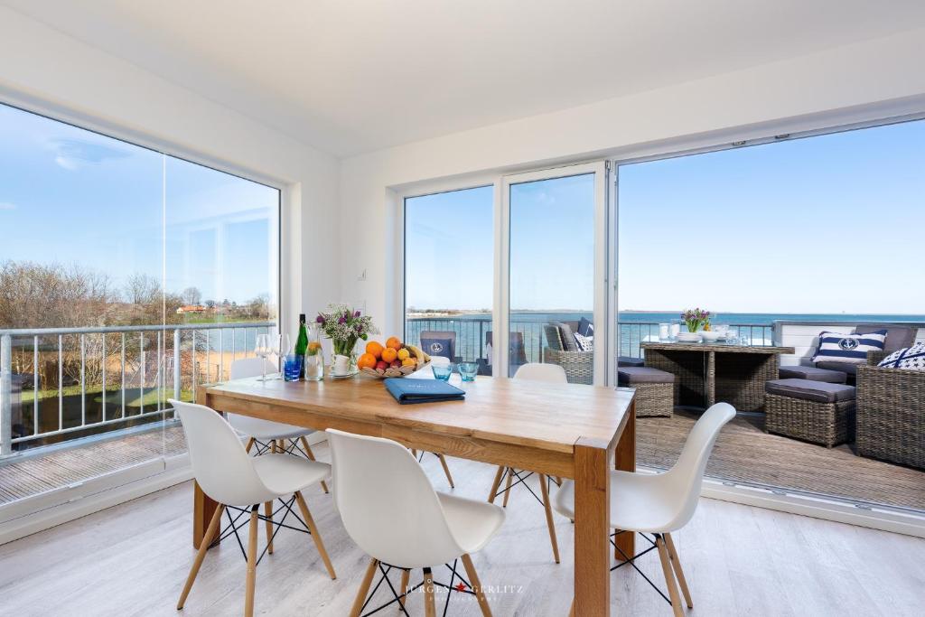 a dining room with white chairs and a wooden table and large windows at An der Ostsee 17 in Olpenitz