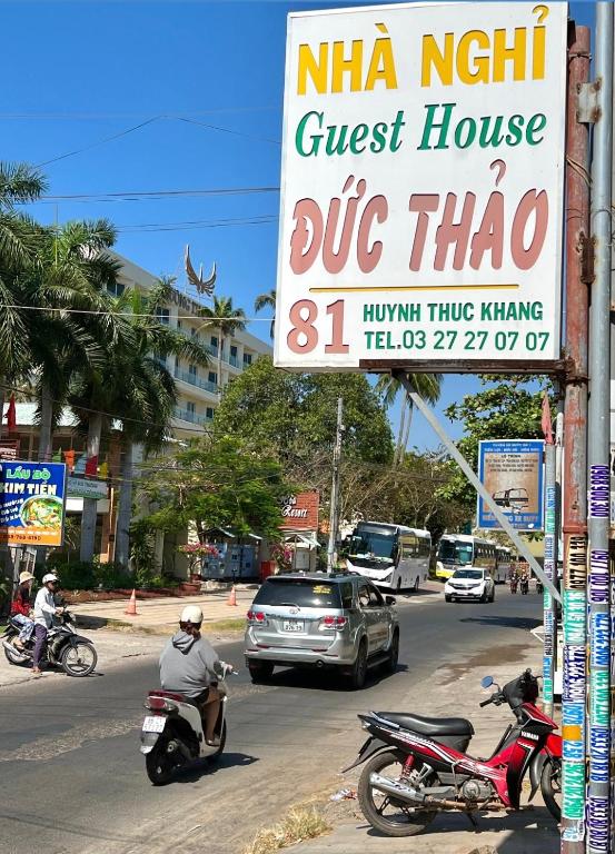 a sign for a guest house on a street with motorcycles at Thao Vi Guest House Duc Thao in Mui Ne