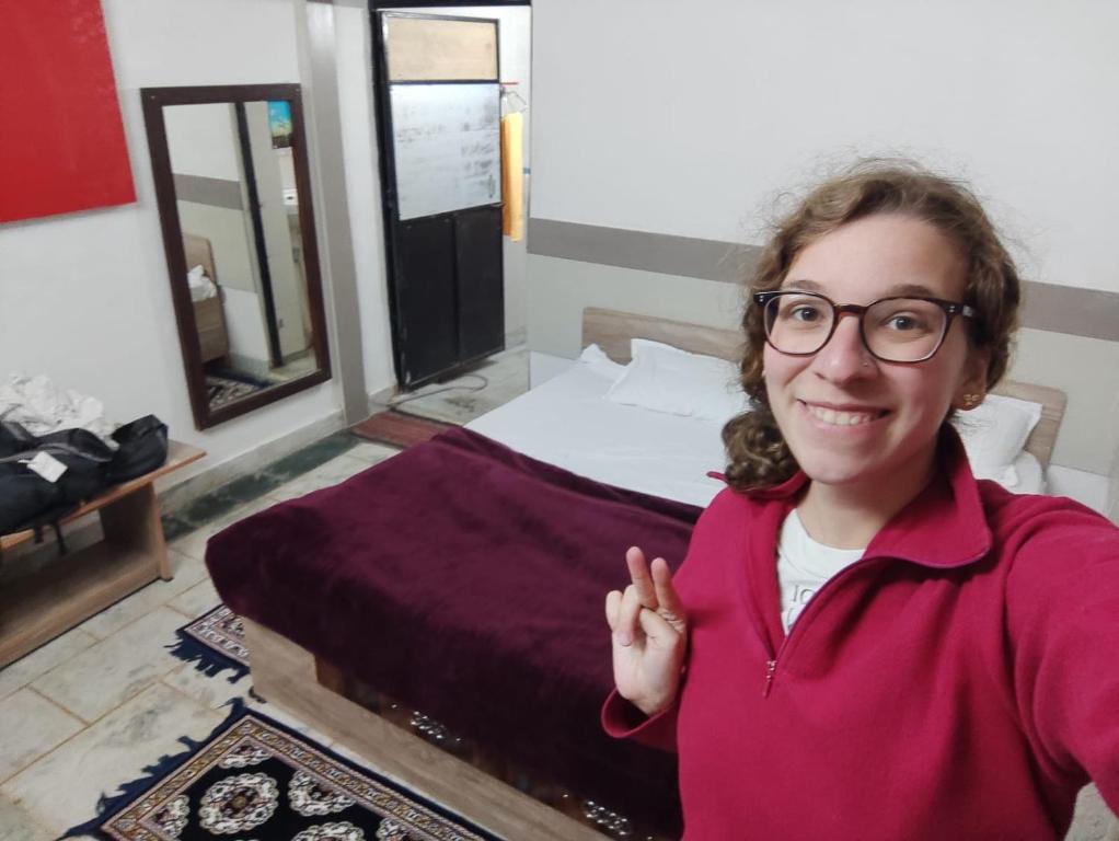 a woman in glasses standing in front of a bed at OP Krishna Homestay in Mathura