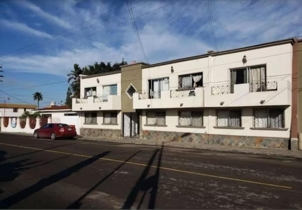 un edificio bianco con un'auto rossa parcheggiata di fronte di Buenaventura. Departamento privado. a Ensenada