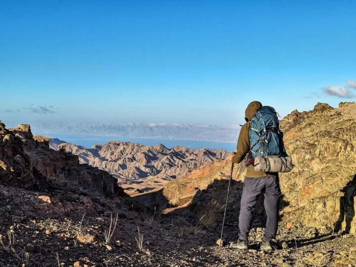 Ein Mann mit einem Rucksack auf einem Berg in der Unterkunft Adventure camping - Organized Trekking from Dana to Petra in Dana