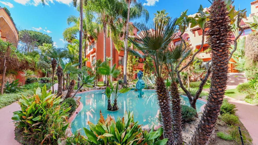 un complejo con una piscina con palmeras y plantas en Secret View Elviria Gardens en Marbella