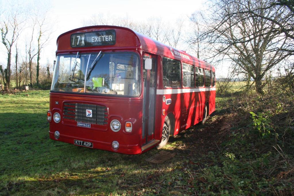 a red bus parked in the grass in a field at Busmans Holiday Anyone in Pontypool