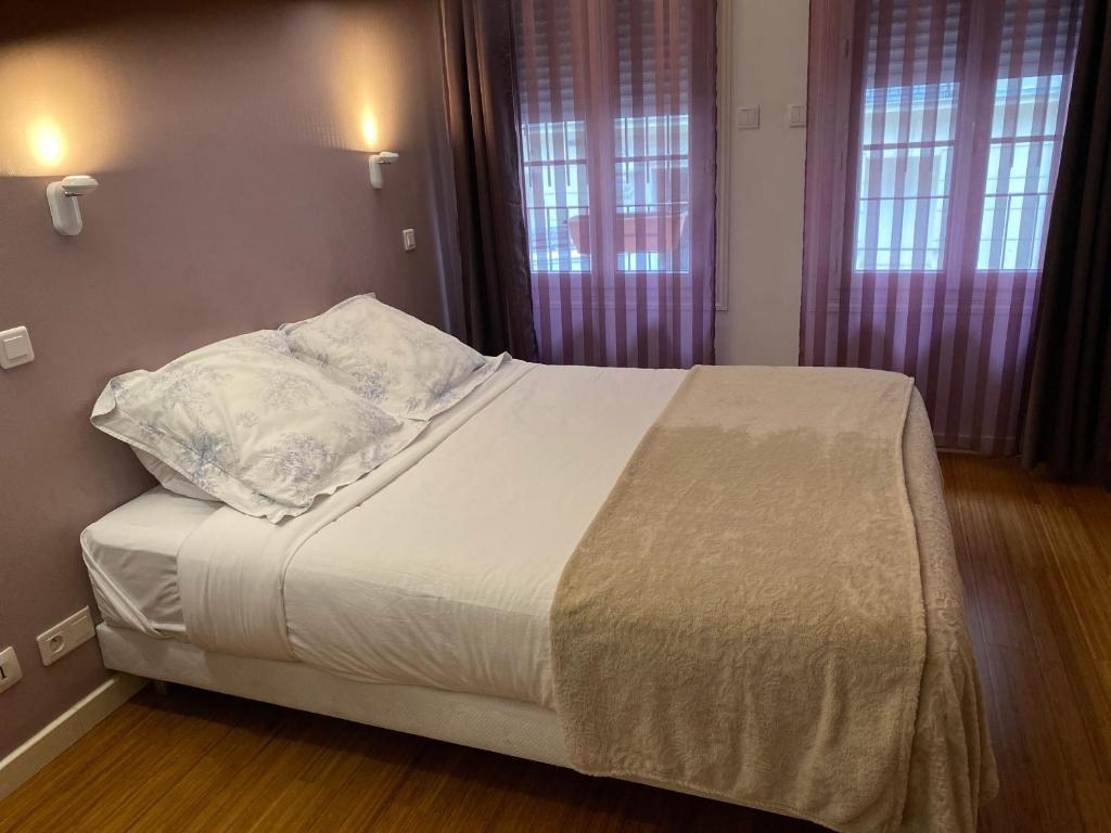 Una cama con sábanas blancas y almohadas en un dormitorio en Hôtel Paris Gambetta en París