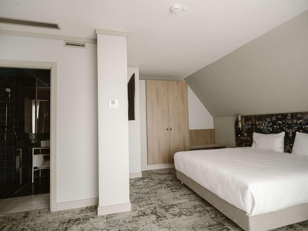 a bedroom with a large white bed and a bathroom at Mercure Sibiu Arsenal in Sibiu