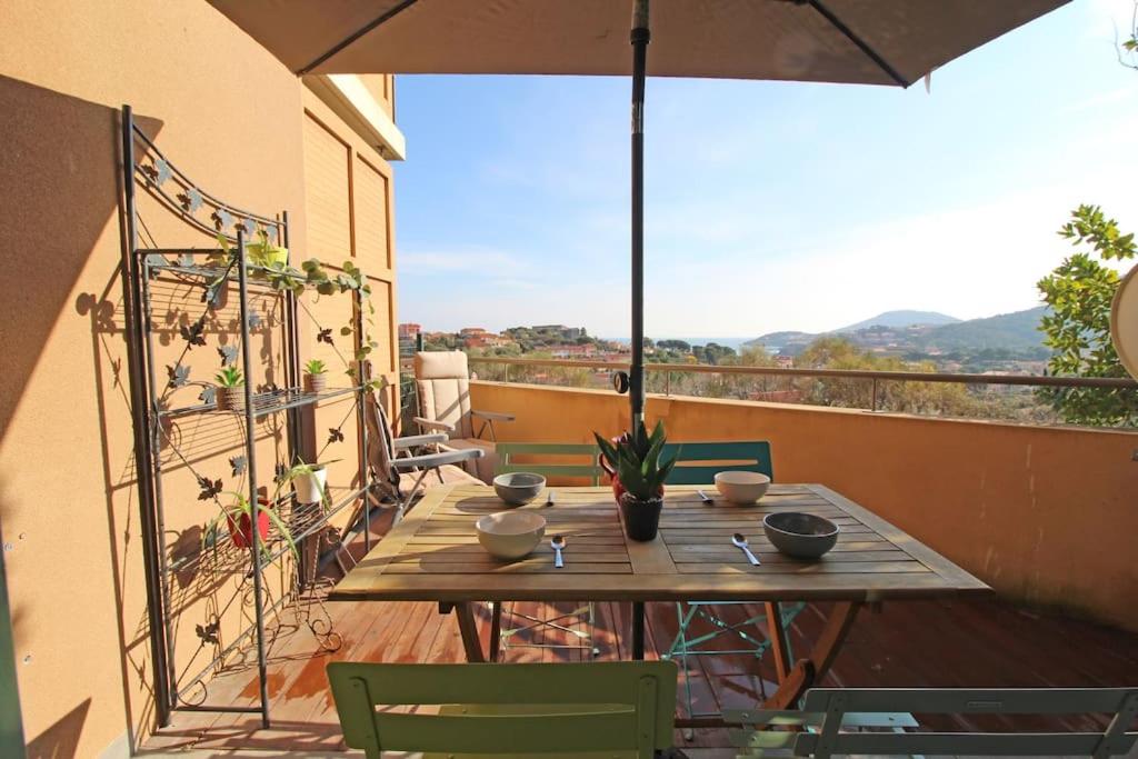 una mesa de madera en un balcón con sombrilla en Joli T2 à 10min à pied du village, parking, vue dégagée, résidence au calme, en Collioure