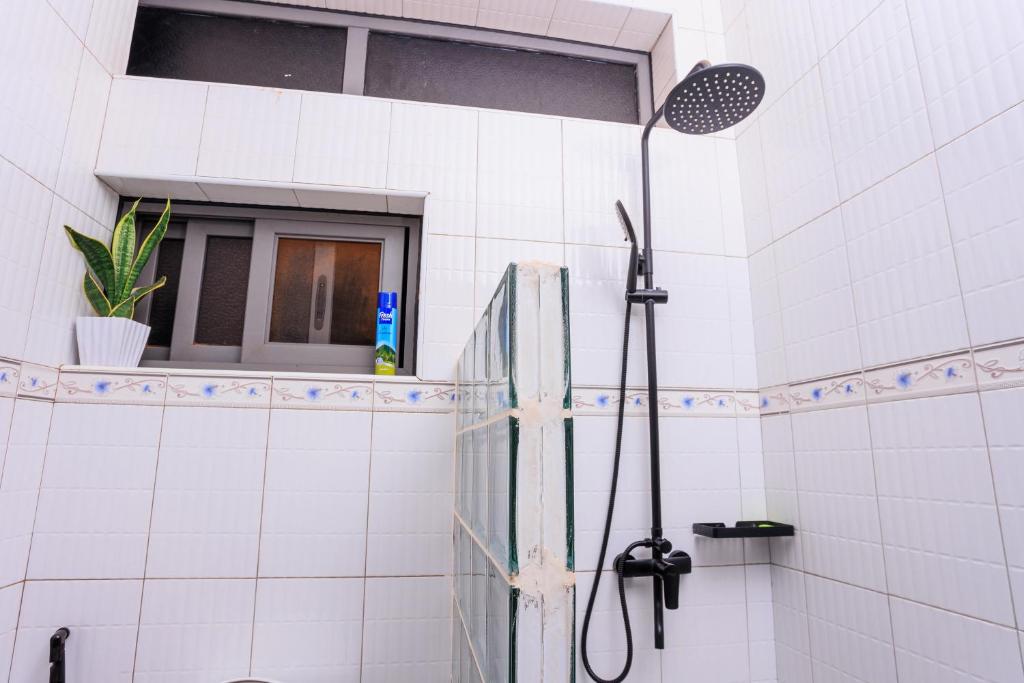 eine Dusche in einem weiß gefliesten Bad mit einem Fenster in der Unterkunft Greenwoods Apartments in Kampala