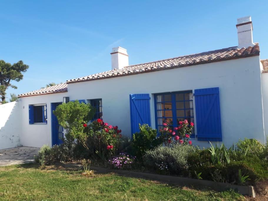 une maison blanche avec des portes bleues et des fleurs dans l'établissement Belle maison familiale à 3 minutes de la plage, à LʼÉpine
