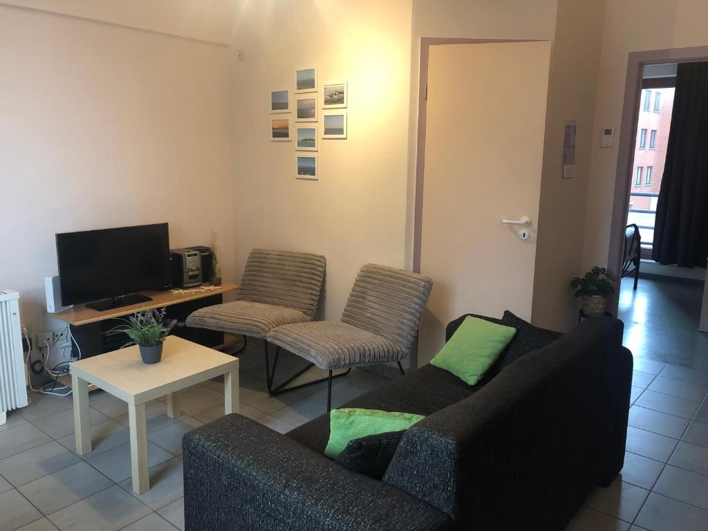 uma sala de estar com um sofá e cadeiras e uma televisão em Duinroos C2 em Koksijde