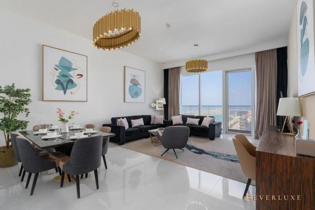 Everluxe Palm Views 3 Bedroom في دبي: غرفة معيشة مع طاولة طعام وأريكة