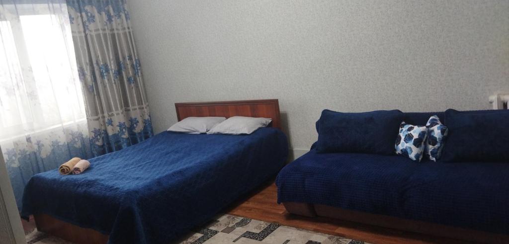 a bedroom with two beds with blue sheets and a window at Квартира in Taraz