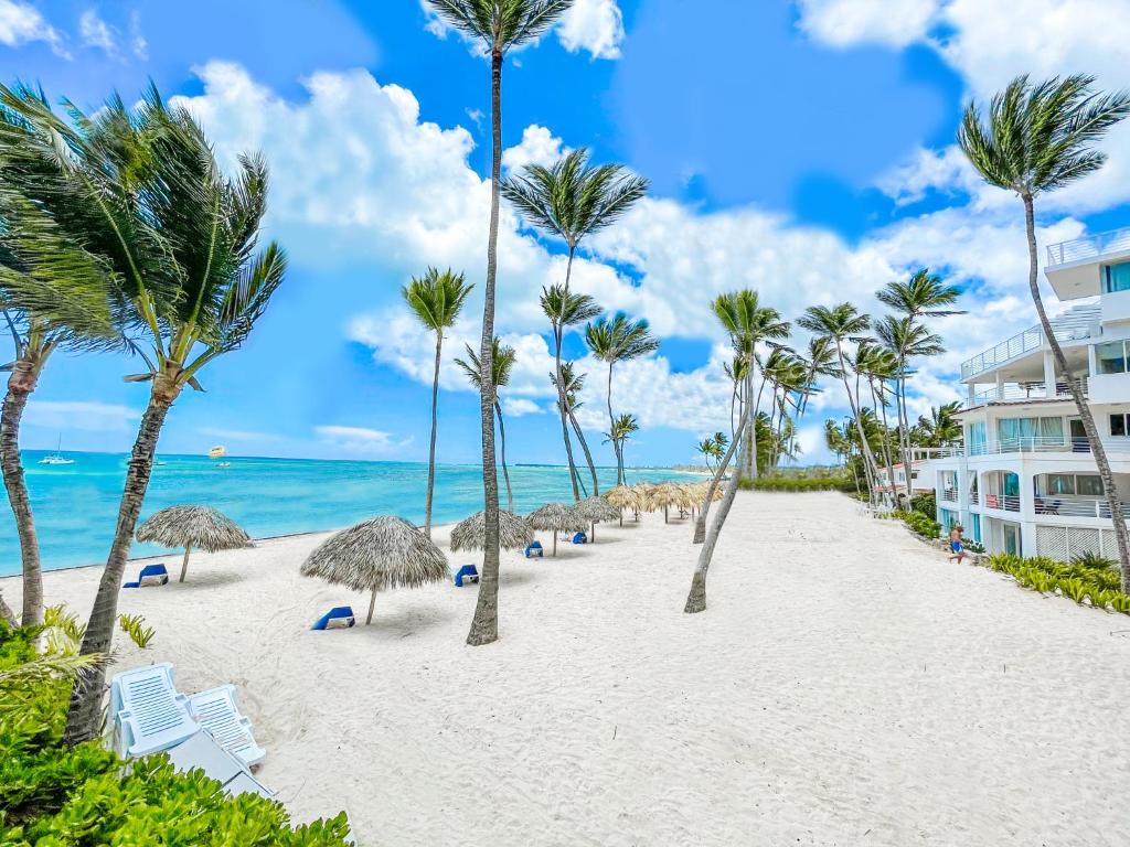 a beach with palm trees and chairs and a building at Holiday Dreams Hotel Los Corales BAVARO WiFi BBQ Parking BEACH CLUB & SPA in Punta Cana