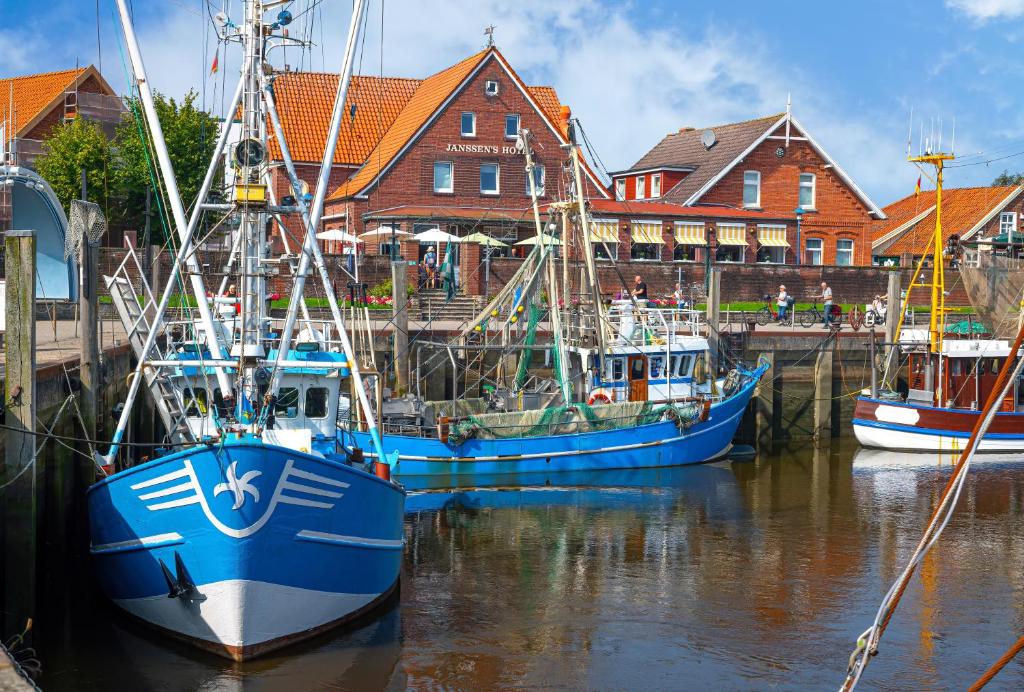 three boats docked in the water in front of houses at Janssens Hotel in Neuharlingersiel