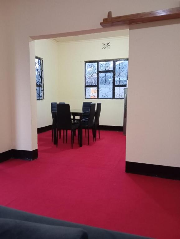 a room with a table and chairs on a red carpet at Kilimanjaro Homestay in Boma la Ngombe