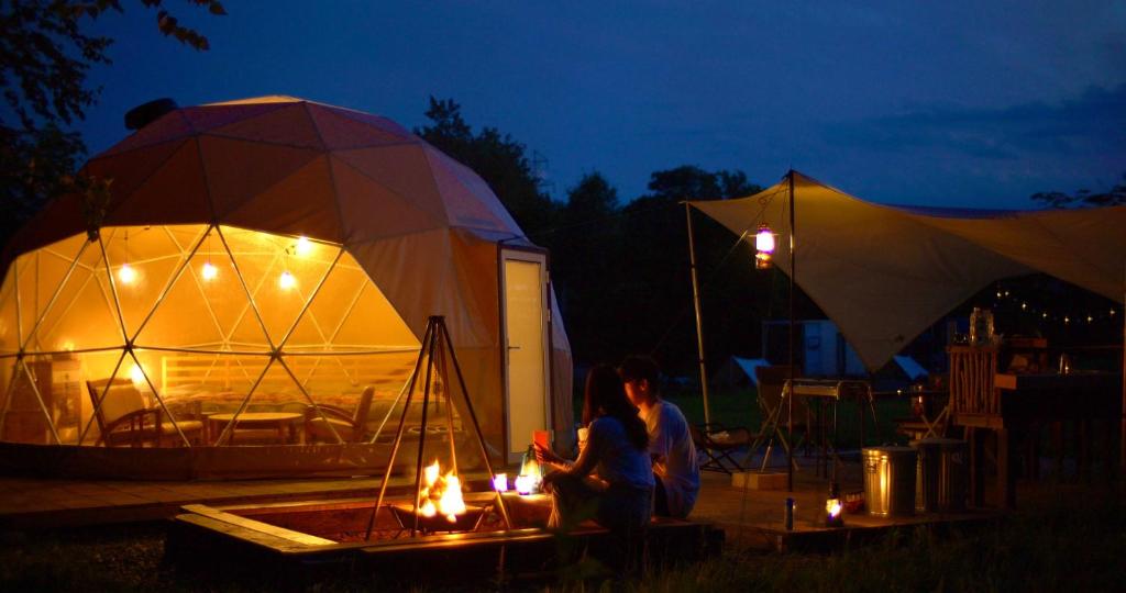 deux personnes assises devant deux tentes la nuit dans l'établissement 真狩村焚き火キャンプ場, à Makkari