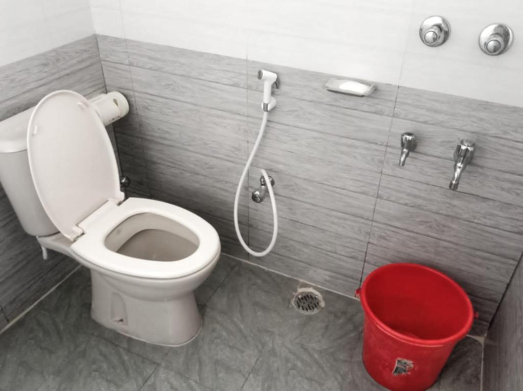 a bathroom with a toilet and a red trash can at Hasnahena 1/F,Dhaka Gurdren City,Adabar,Mohammadpur in Dhaka