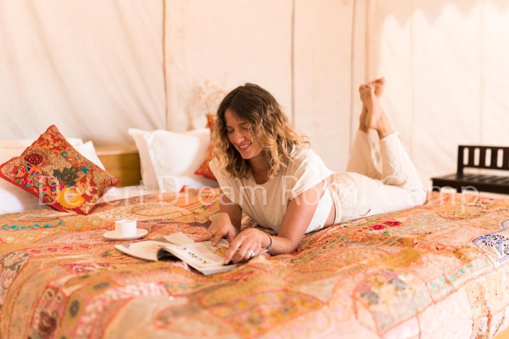 Desert Dream Royal Camp with Pool في جيلسامر: امرأة مستلقية على سرير تقرأ كتابا