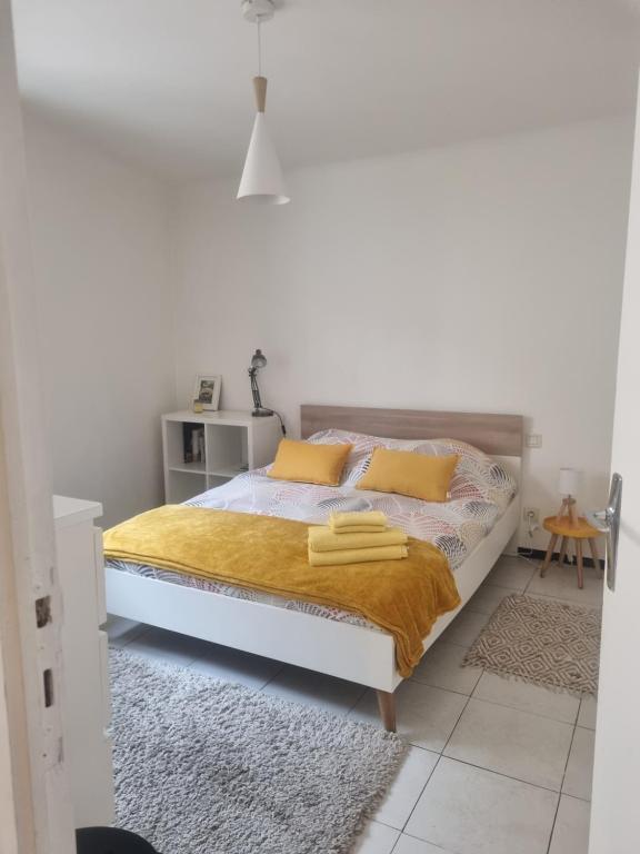a white bedroom with a bed with yellow pillows at Appartement coquet Le Boulou in Le Boulou