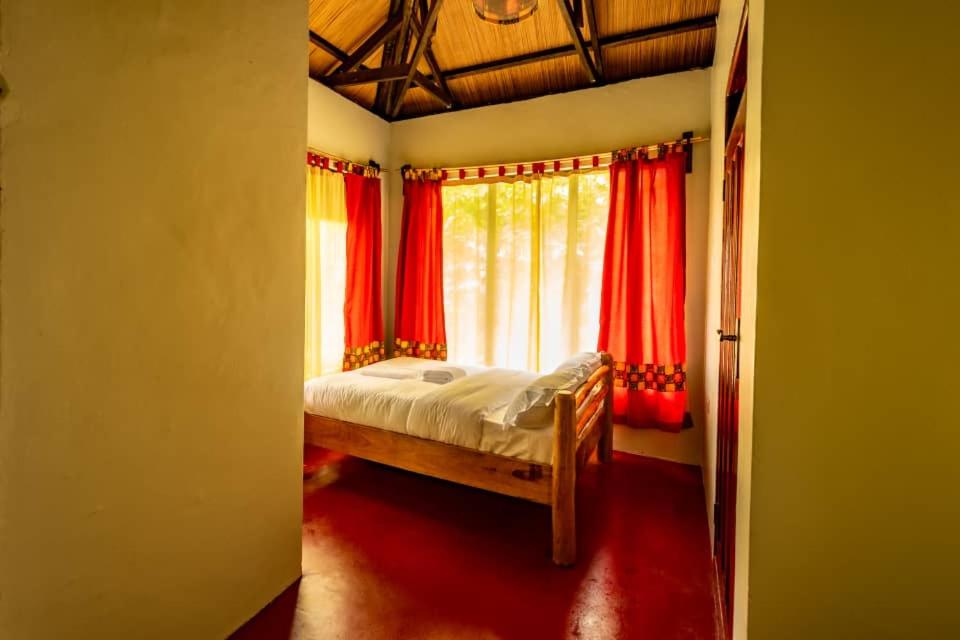 a bedroom with a bed with red curtains and a window at Mise cave lodge in Kapchorwa