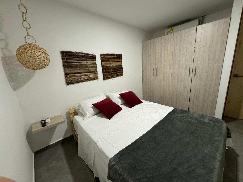 um quarto com uma cama com lençóis brancos e almofadas vermelhas em Apartamentos Area Medica Imbanaco em Cali