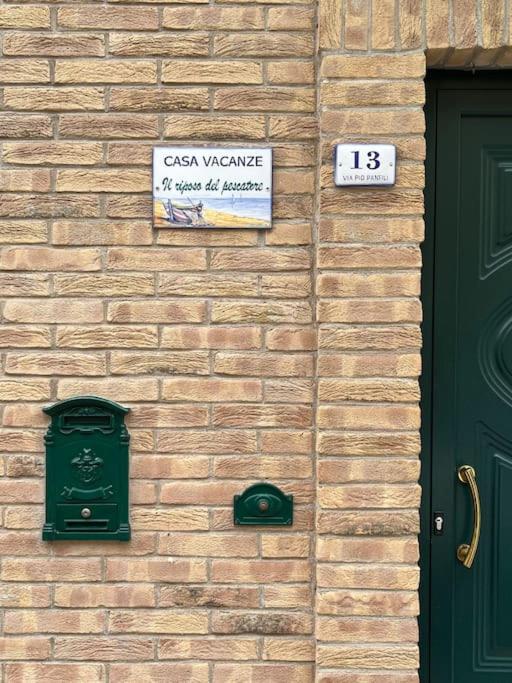 una pared de ladrillo con una puerta verde y un cartel en Casa “il riposo del pescatore”, en Porto San Giorgio