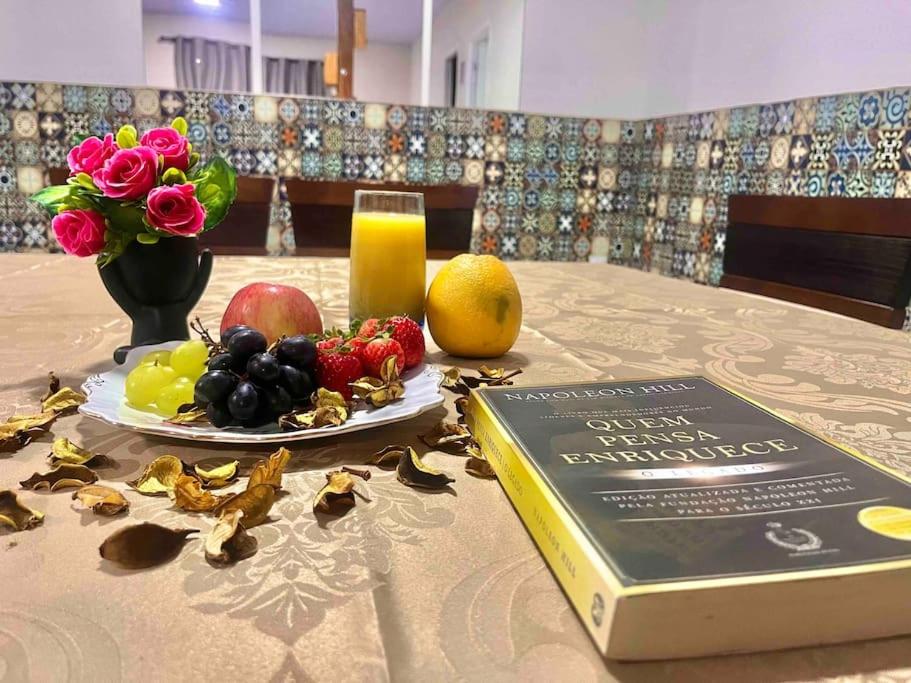 een boek op een tafel met een bord fruit bij Conforto e Espaço no Coração de Balneário in Balneário Camboriú