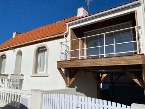 ein weißes Haus mit einem Holzbalkon und einem Zaun in der Unterkunft Charmante Maison, terrasse vue mer in Les Sables-dʼOlonne