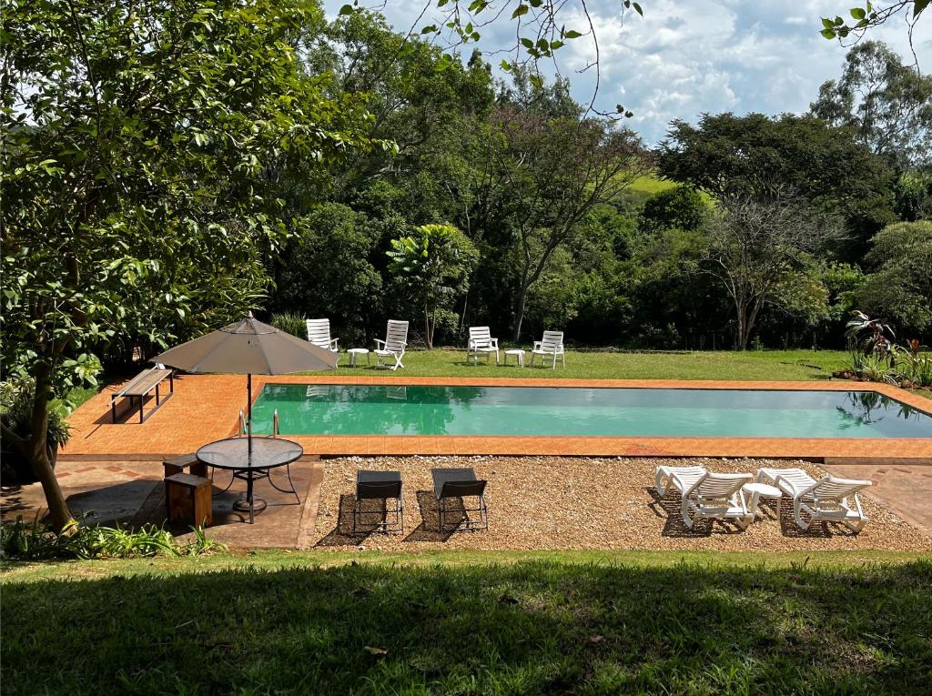 a swimming pool with chairs and a table and an umbrella at Hospedaria do Feno in Brotas