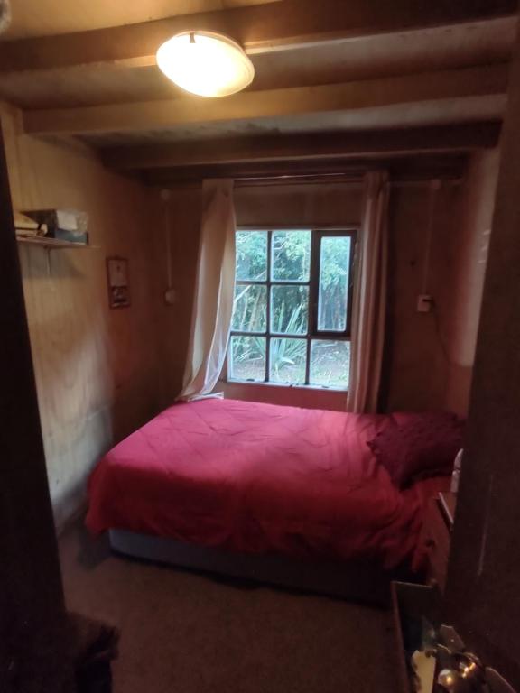 1 dormitorio con cama roja y ventana en La recta del 14, en Agua Fría