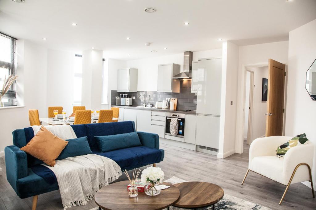 Cityscape 2-BR - Leicester's Premier Urban Retreat في ليستر: غرفة معيشة مع أريكة زرقاء ومطبخ