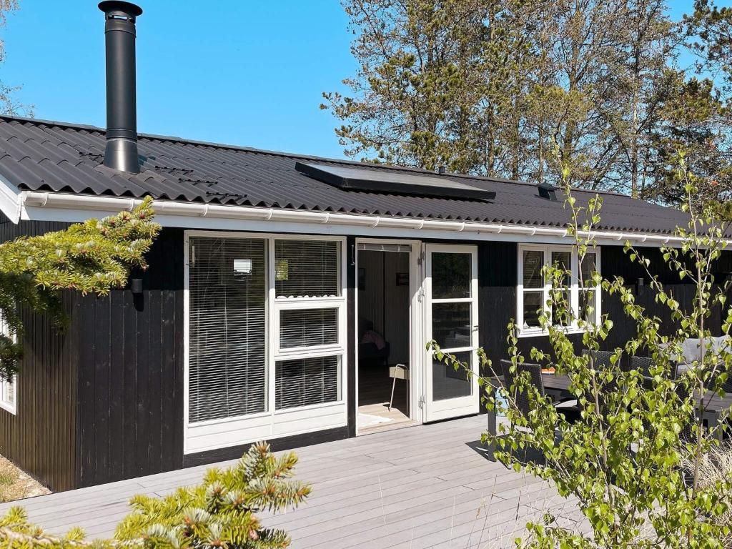 uma pequena casa preta com um alpendre e um deque em Holiday home Ålbæk LXXXV em Ålbæk