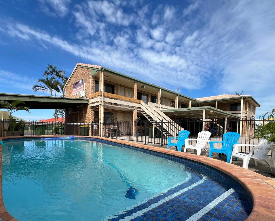 a swimming pool with blue chairs and a house at Golden Beach Motor Inn, Caloundra in Caloundra