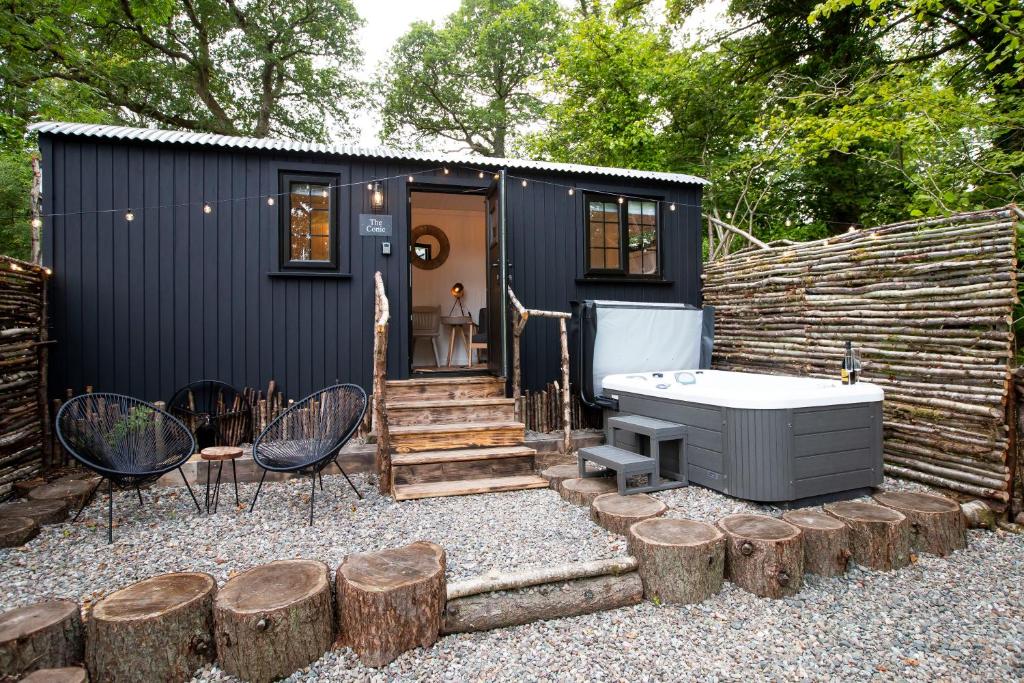 ein schwarzes winziges Haus mit einem Whirlpool und einigen Bäumen in der Unterkunft The Mar Huts - The Conic Hut in Drymen